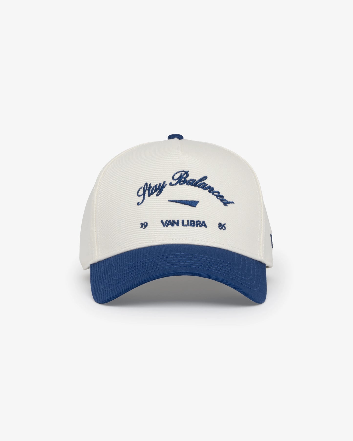 Van Libra Bone/Indigo (cream and blue) structured cap with bone colored crown and indigo colored brim. Features blue embroidered text “Stay Balanced” with abstract triangle graphic on the front, “1986” and “VAN LIBRA” details, and “VL” stitched on the side, finished with an adjustable indigo snapback closure at the back.