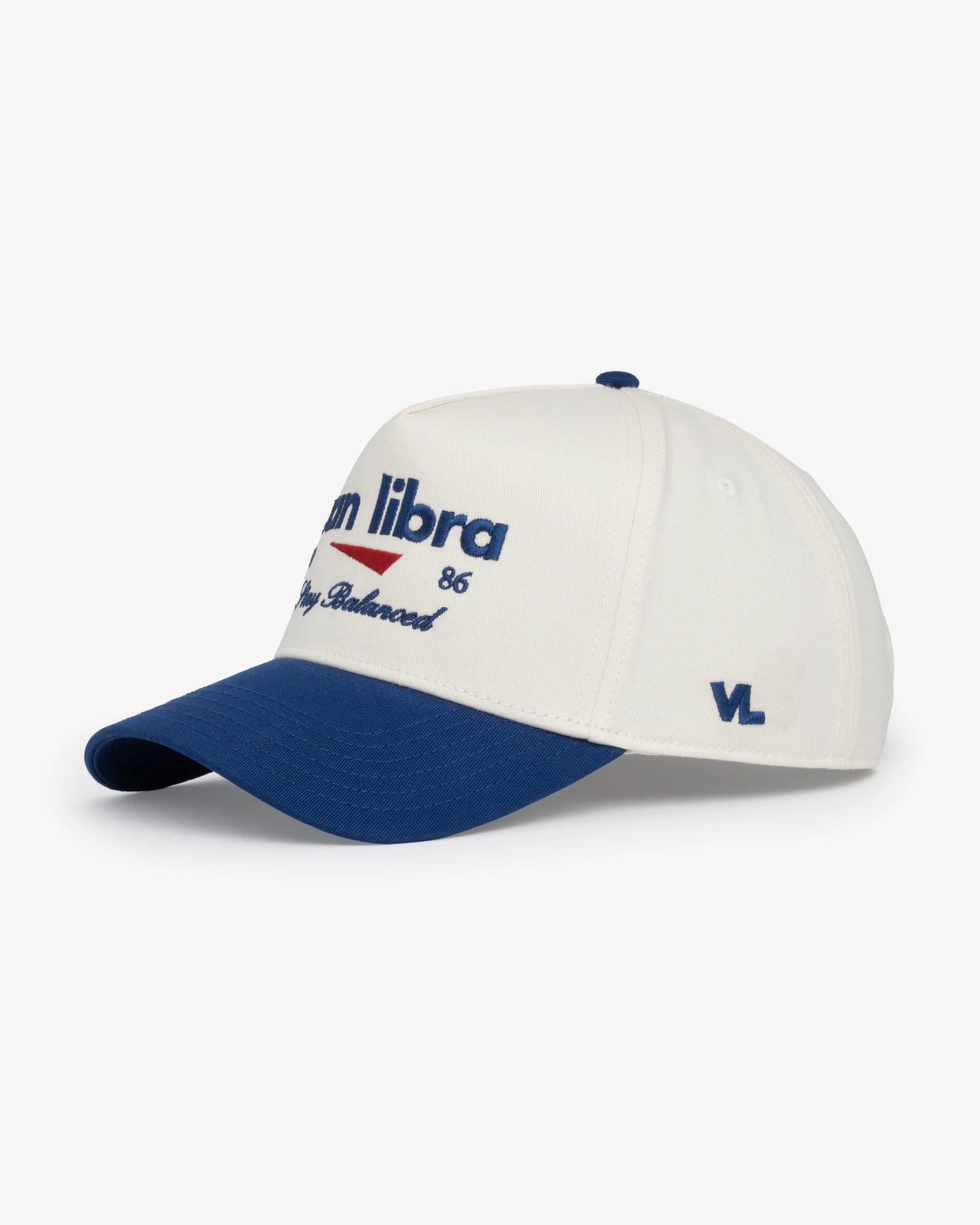 Van Libra Bone/Indigo (cream and blue) structured cap with bone colored crown and indigo colored brim. Features blue embroidered text “van libra” with red abstract triangle graphic on the front, blue “1986” and “Stay Balanced” lettering on the front, plus “VL” stitched on the side, finished with an adjustable indigo snapback closure at the back.