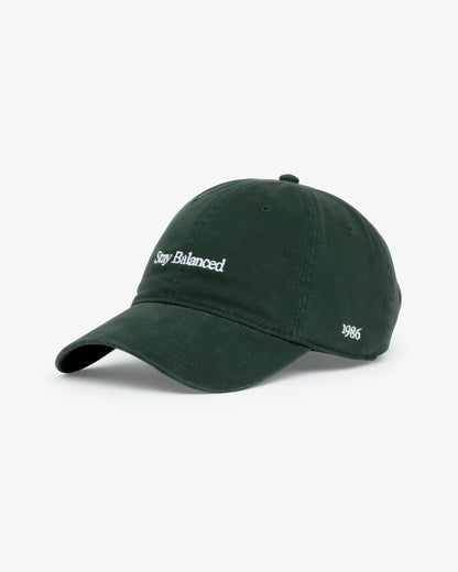 Van Libra Forest (dark green) dad hat with white embroidered text “Stay Balanced” on the front, “1986” stitched on the side, and “VAN LIBRA” on the back above an adjustable strap with brass buckle.