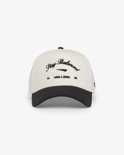 Van Libra Bone/Carbon (cream and dark gray) structured cap with bone colored crown and carbon colored brim. Features black embroidered text “Stay Balanced” with abstract triangle graphic on the front, “1986” and “VAN LIBRA” details, and “VL” stitched on the side, finished with an adjustable carbon colored snapback closure at the back.