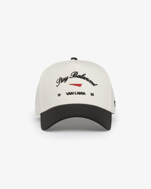 Van Libra Bone/Carbon (cream and dark gray) structured cap with bone colored crown and carbon colored brim. Features black embroidered text “Stay Balanced” with red abstract triangle graphic on the front, black “1986” and “VAN LIBRA” details, and “VL” stitched on the side, finished with an adjustable carbon colored snapback closure at the back.