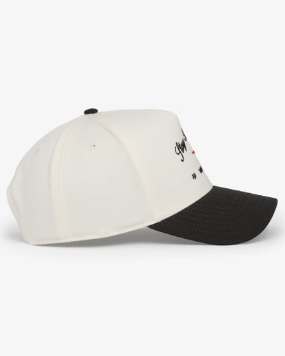 Van Libra Bone/Carbon (cream and dark gray) structured cap with bone colored crown and carbon colored brim. Features black embroidered text “Stay Balanced” with red abstract triangle graphic on the front, black “1986” and “VAN LIBRA” details, and “VL” stitched on the side, finished with an adjustable carbon colored snapback closure at the back.