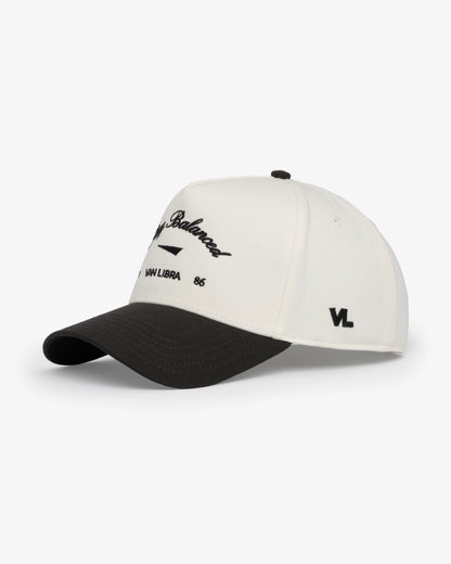 Van Libra Bone/Carbon (cream and dark gray) structured cap with bone colored crown and carbon colored brim. Features black embroidered text “Stay Balanced” with abstract triangle graphic on the front, “1986” and “VAN LIBRA” details, and “VL” stitched on the side, finished with an adjustable carbon colored snapback closure at the back.