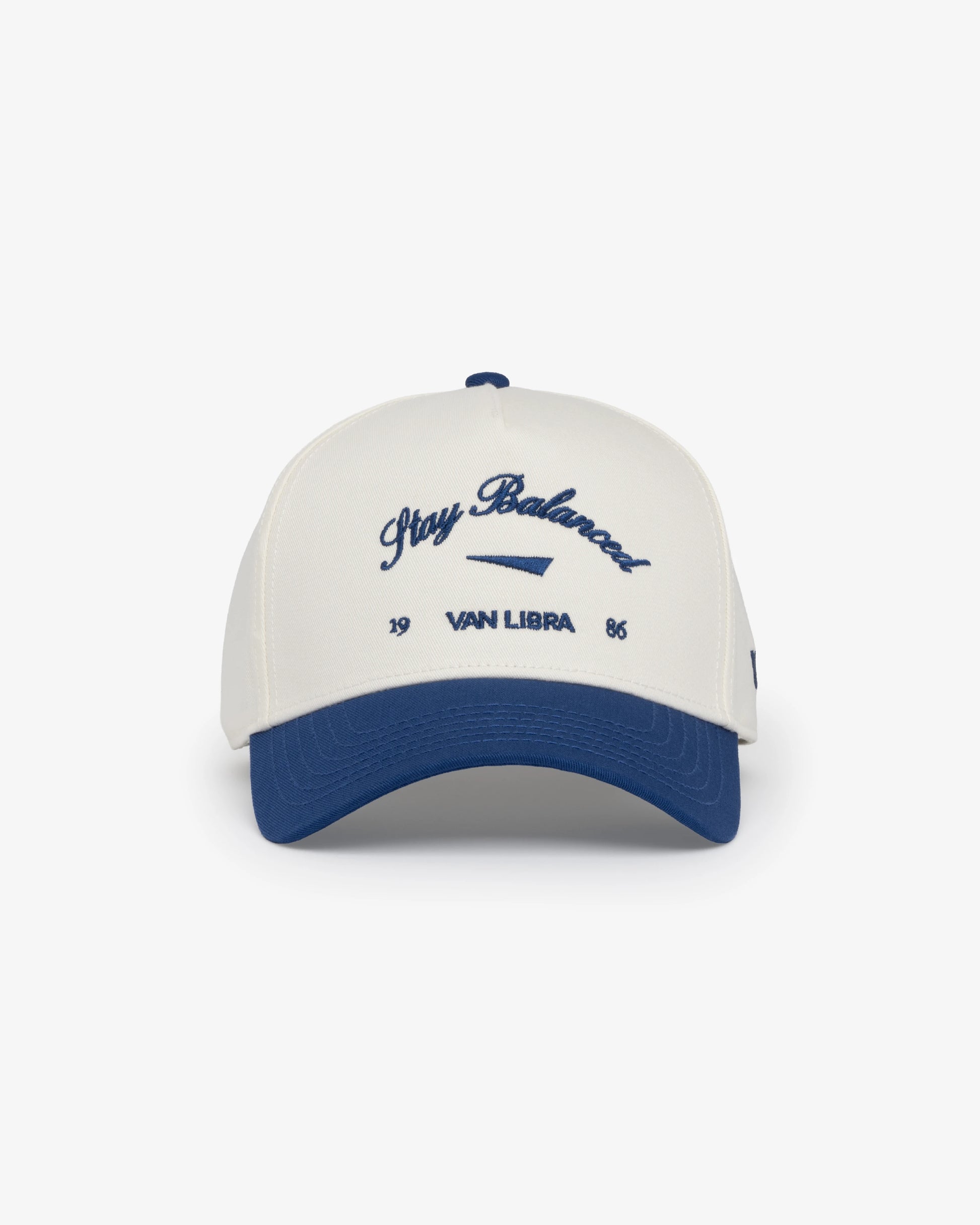 Van Libra Bone/Indigo (cream and blue) structured cap with bone colored crown and indigo colored brim. Features blue embroidered text “Stay Balanced” with abstract triangle graphic on the front, “1986” and “VAN LIBRA” details, and “VL” stitched on the side, finished with an adjustable indigo snapback closure at the back.