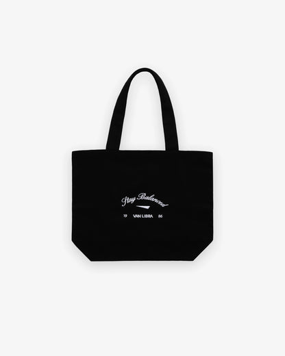 Van Libra Blackwood (black) canvas tote bag with white embroidery. Features “Stay Balanced” text above an abstract triangle graphic, with “VAN LIBRA” and the numbers “19” and “86” stitched below.