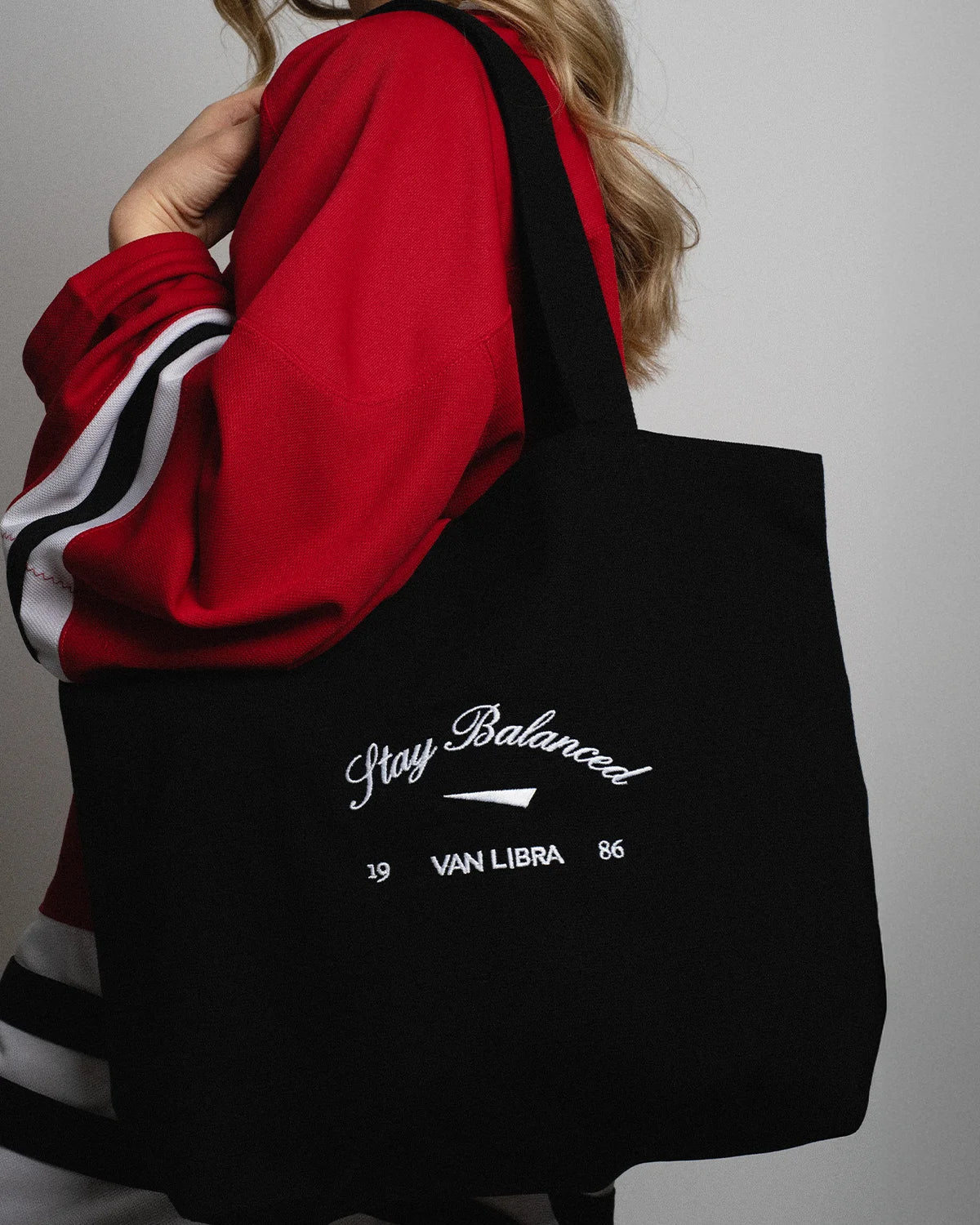 Van Libra Blackwood (black) canvas tote bag with white embroidery. Features “Stay Balanced” text above an abstract triangle graphic, with “VAN LIBRA” and the numbers “19” and “86” stitched below.