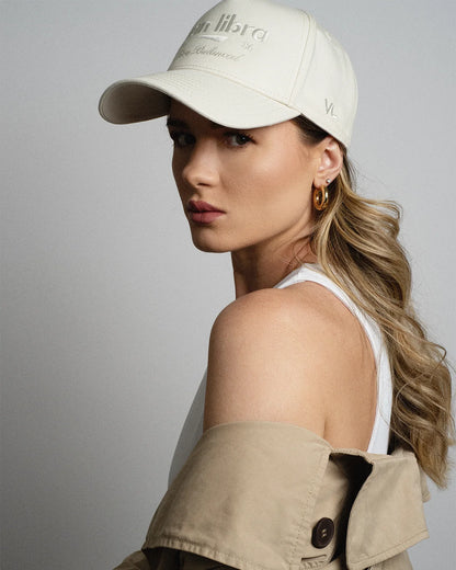Van Libra Ivory (cream) structured cap with ivory crown and brim. Features cream colored embroidered text “van libra” with abstract triangle graphic on the front, “1986” and “Stay Balanced” lettering on the front, plus “VL” stitched on the side, finished with an adjustable ivory snapback closure at the back.